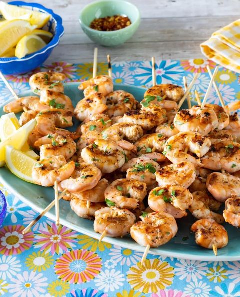 grilled shrimp skewers with lemon wedges and red pepper flakes in bowl