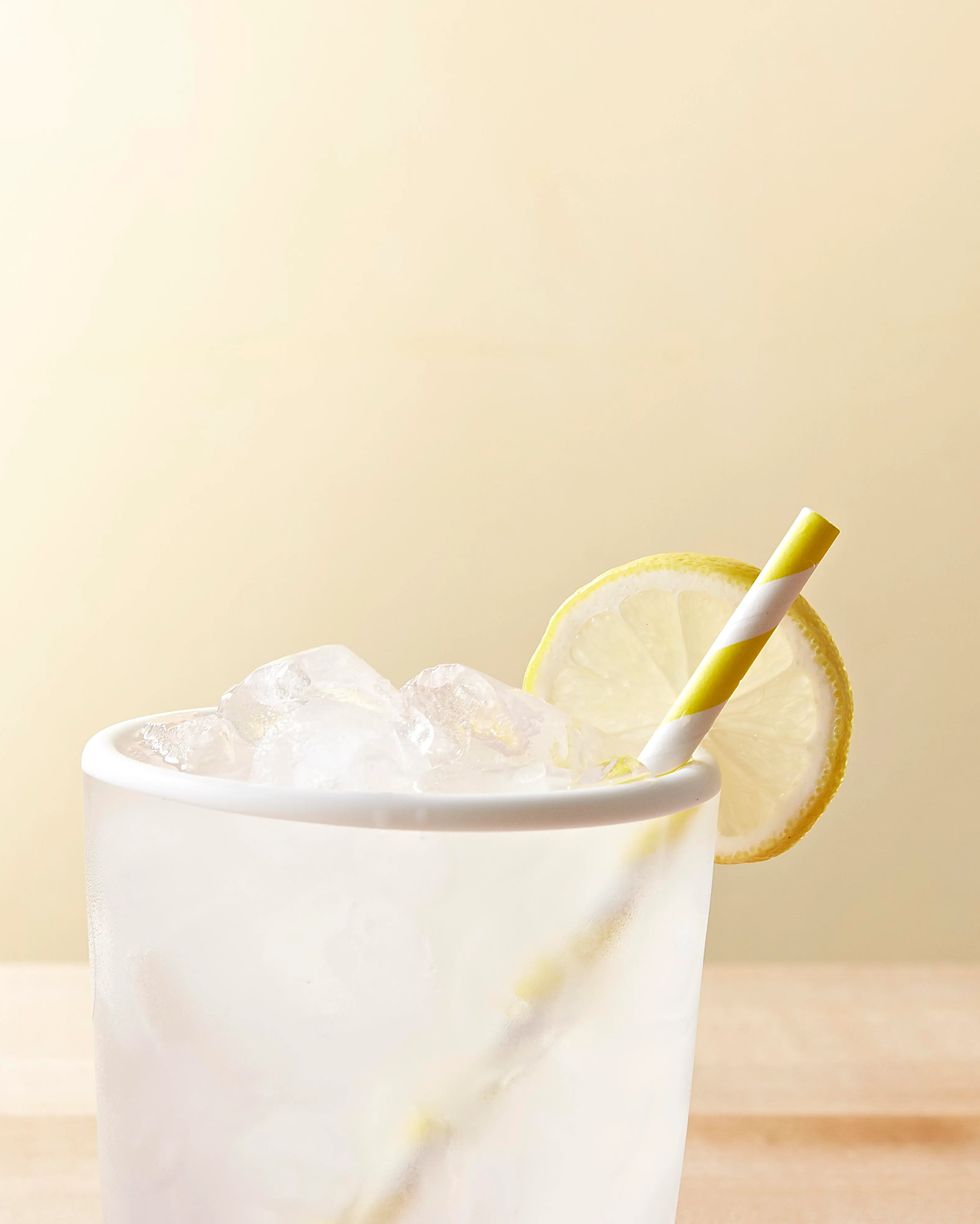 mason jar lemonade in a clear cup with a yellow striped paper straw and a lemon slice for garnish