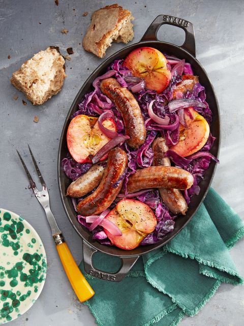 seared sausage cabbage and apple halves arranged in an oval shaped cast iron baking dish