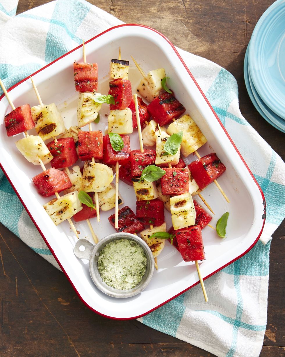 grilled watermelon and halloumi kebabs stacked on a tray with a small bowl of basil salt for serving