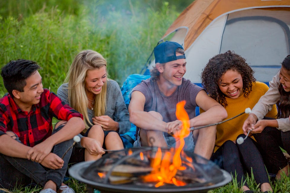 teenage friends roasting marshmallows over a campfire and laughing