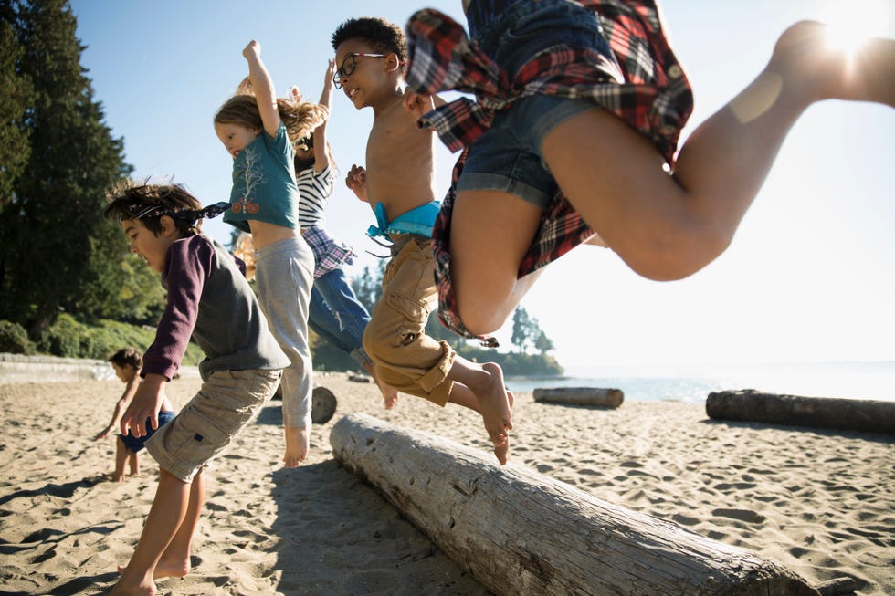 Boy and girl friends jumping over log on sunny beach