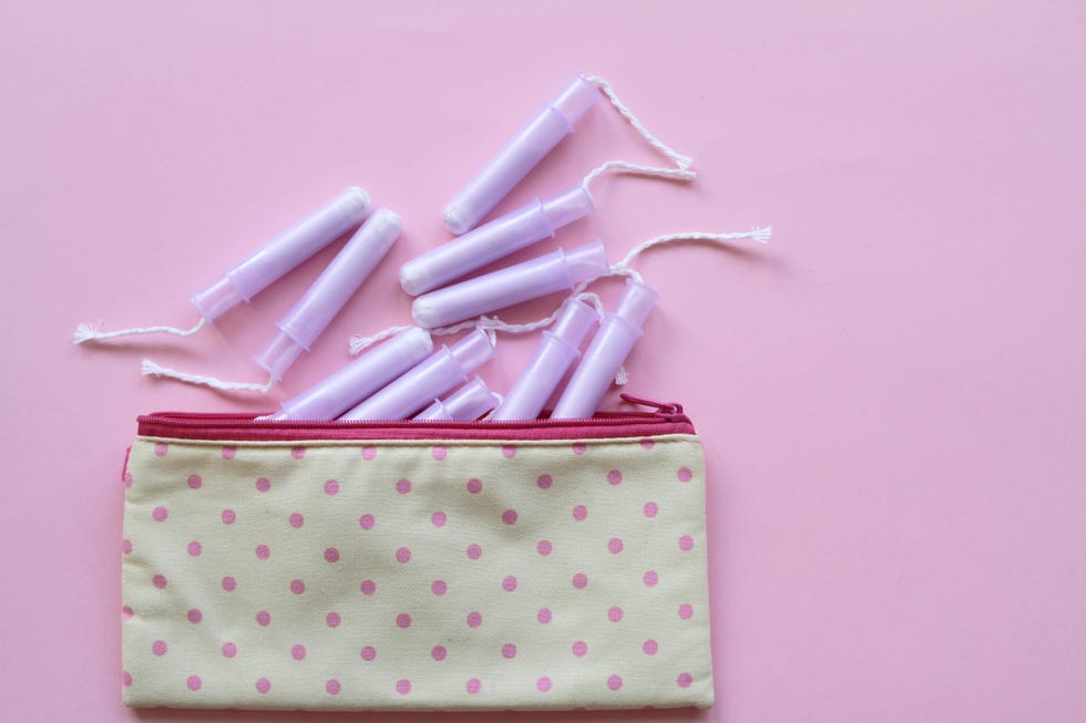 tas menstruasi dengan tampon kapas, pembalut wanita dan pil dengan latar belakang merah muda
