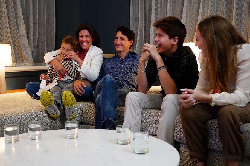 justin trudeau lounges on a deep sofa while sitting next to his wife and three children, everyone is smiling