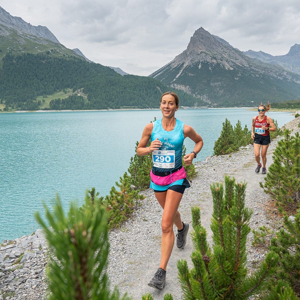 runners competing along a path by a lake surrounded by mountains