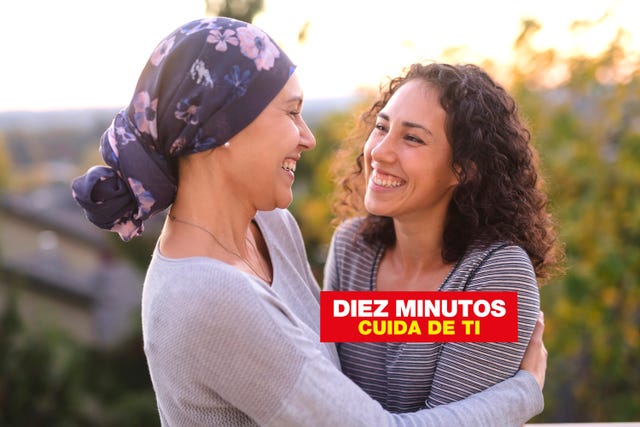 a beautiful young woman fighting cancer and wearing a head wrap embraces her sister they are vibrantly smiling at each other they are standing outdoors and there are mountains and trees in the background