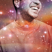 a smiling man from the nose to chest is shown in a starry rainbow sky