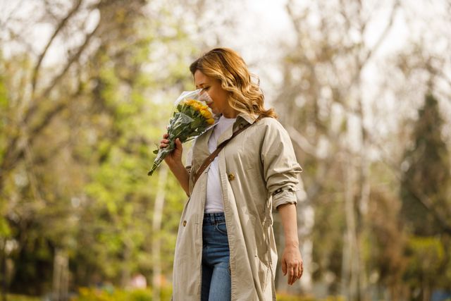 candid shot of woman walking through the park and smelling a bouquet of yellow roses