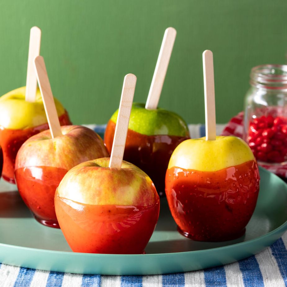 candied apples coated with red cinnamon candy with popsicle sticks on blue striped linen with cinnamon candy in the background