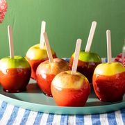 candied apples coated with red cinnamon candy with popsicle sticks on blue striped linen with cinnamon candy in the background