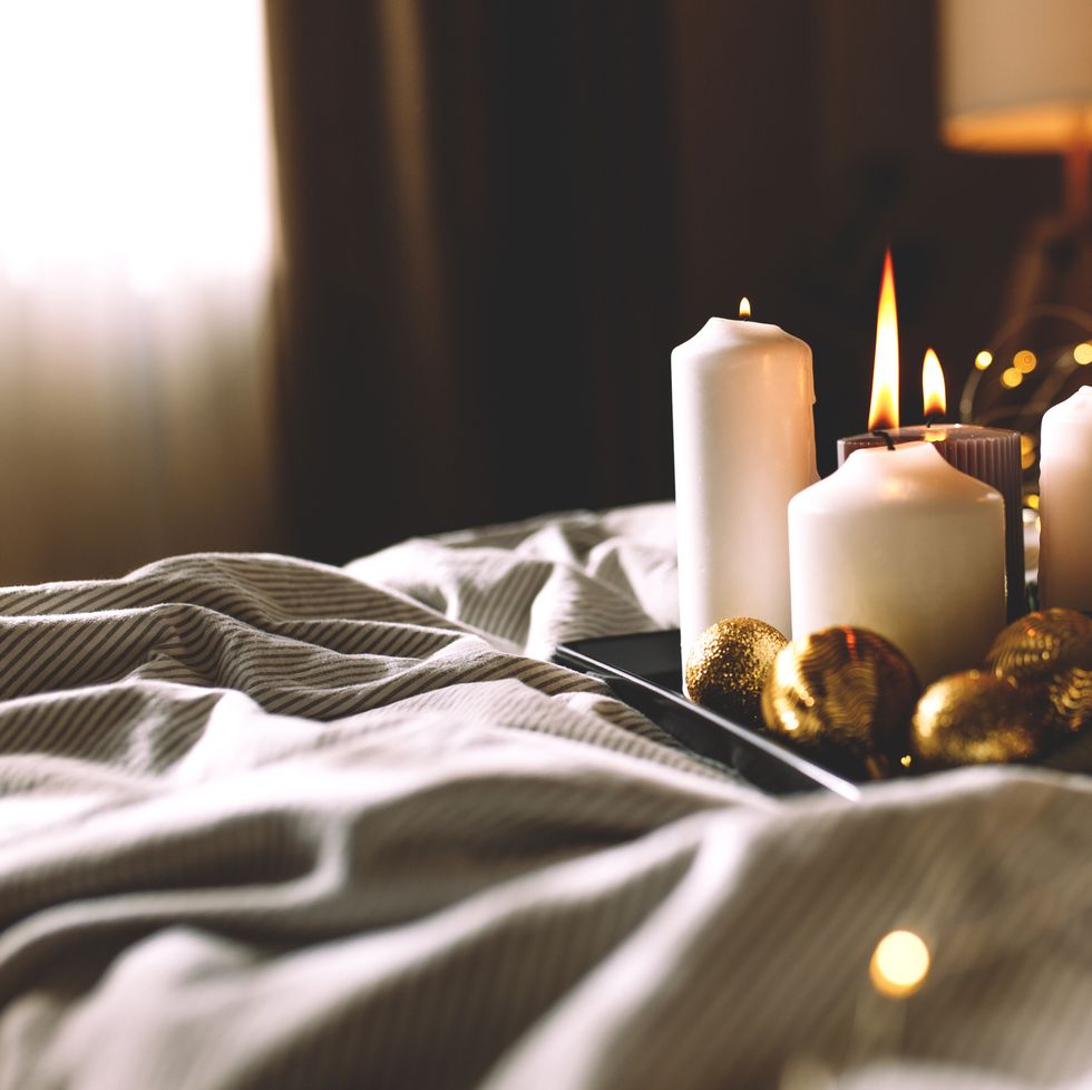 candles on the bed focus cosy bedroom interior with bed, plaids, flashlights, candles and dark walls christmas decoration white bedding sheets with striped blanket and pillow hygge concept