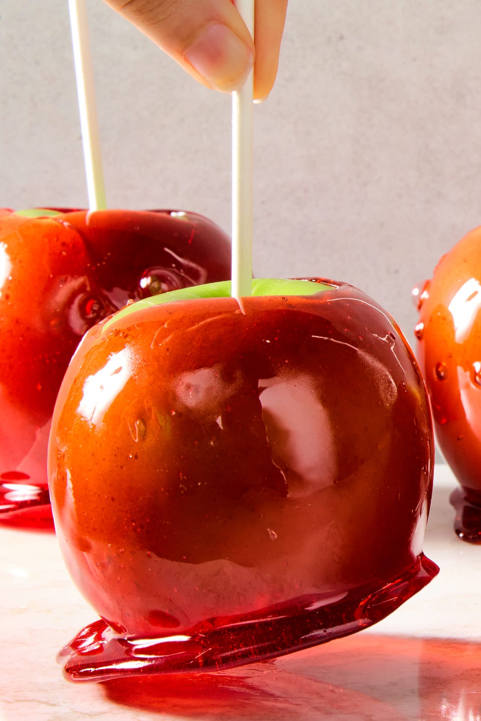 green apples with a red candy coating and a popsicle stick