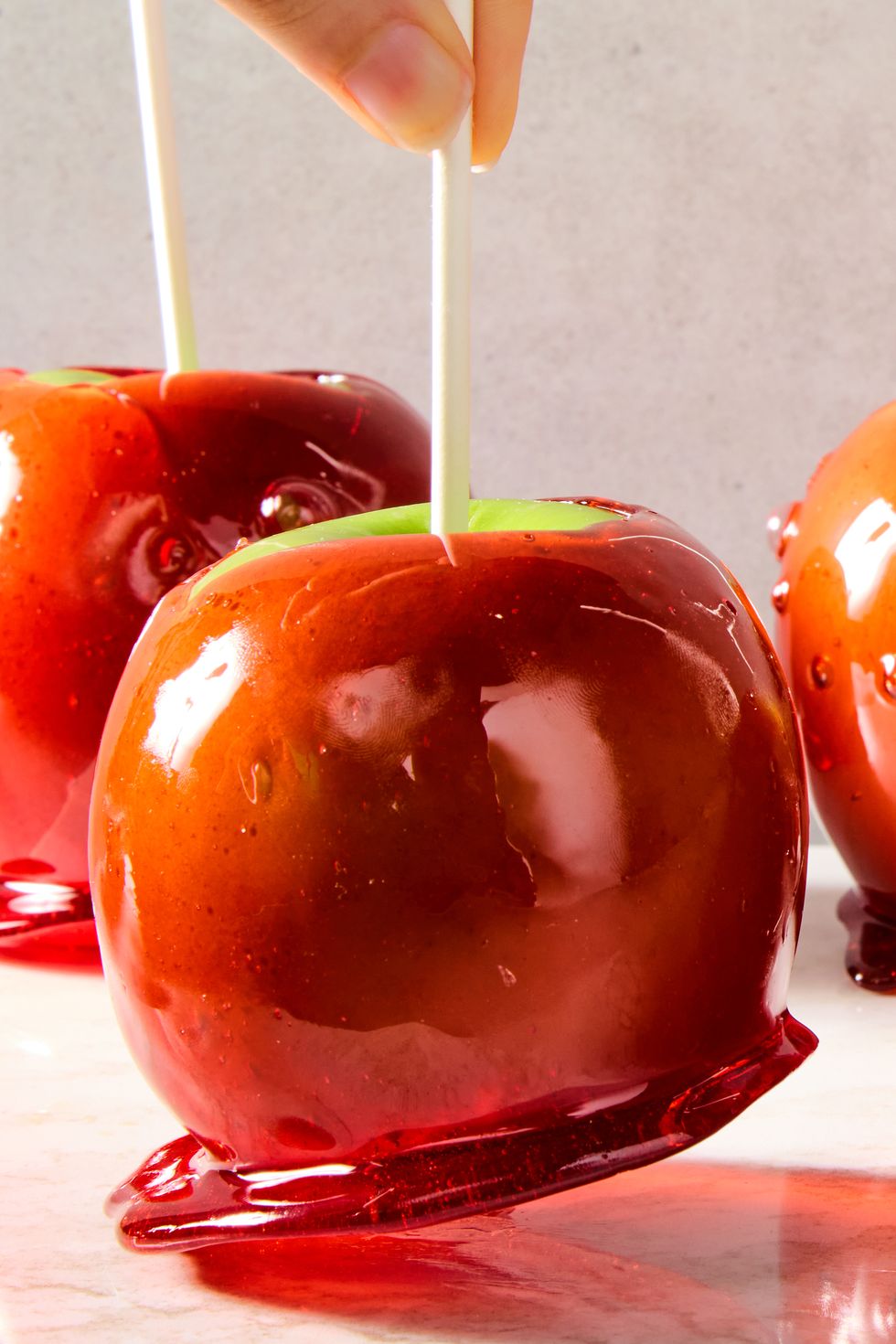 green apples with a red candy coating and a popsicle stick