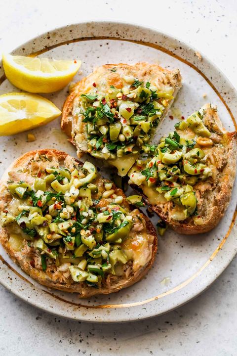 two cheesy tuna toasts with olive salsa on a plate with lemon wedges