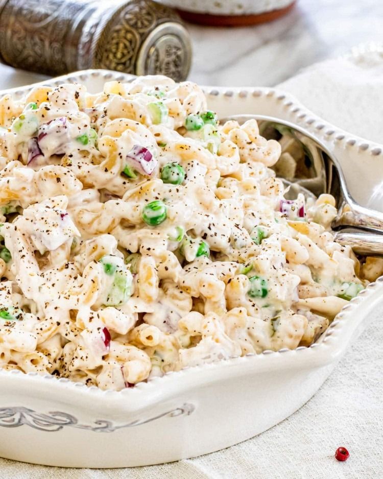 tuna macaroni salad in a white serving dish with silver serving utensils