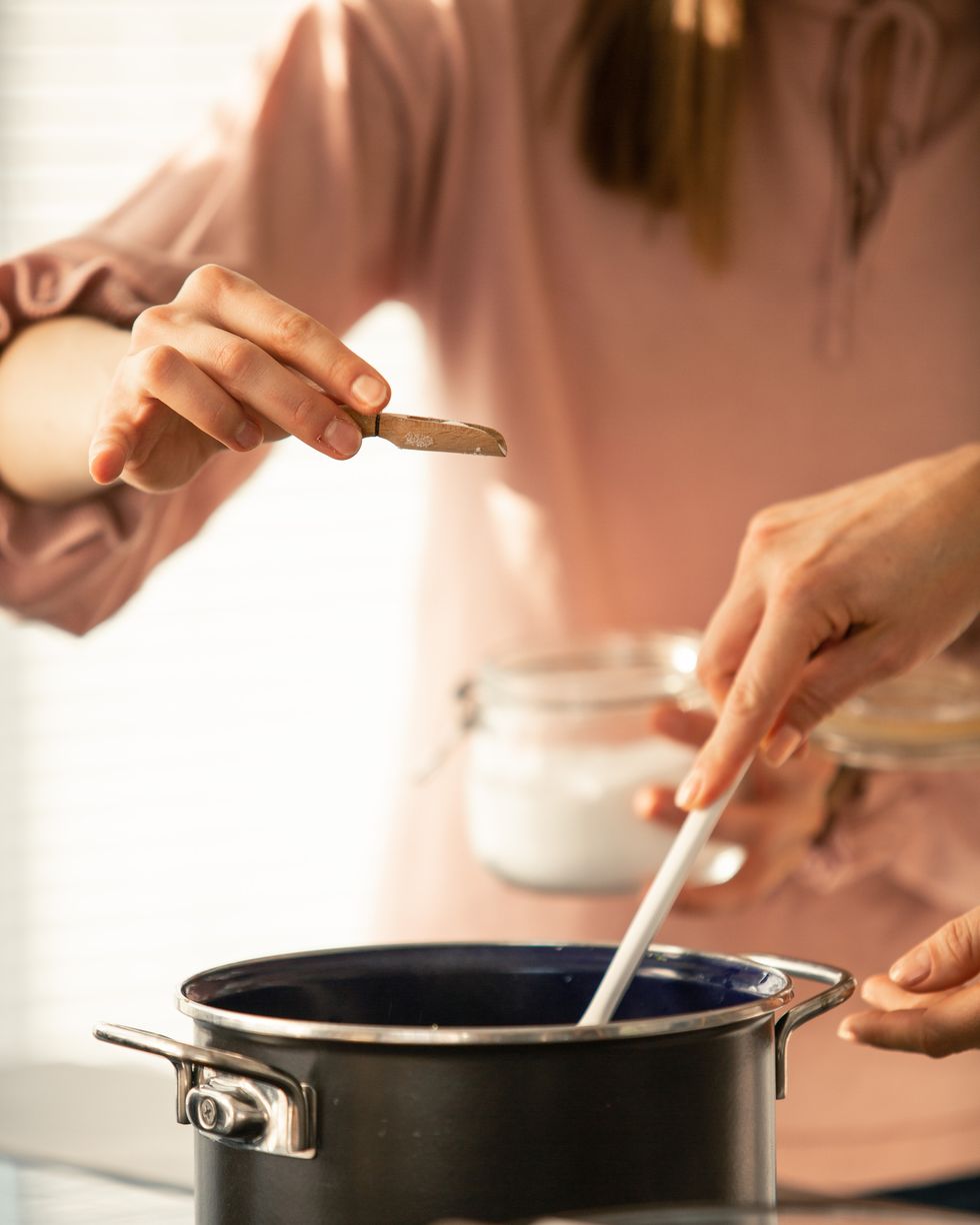 una mujer sostiene un salero sobre una cacerola en la cocina de su casa