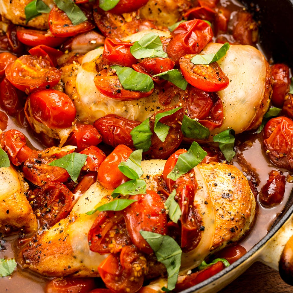 chicken breasts cooked in a skillet with cherry tomatoes, mozzarella, and basil
