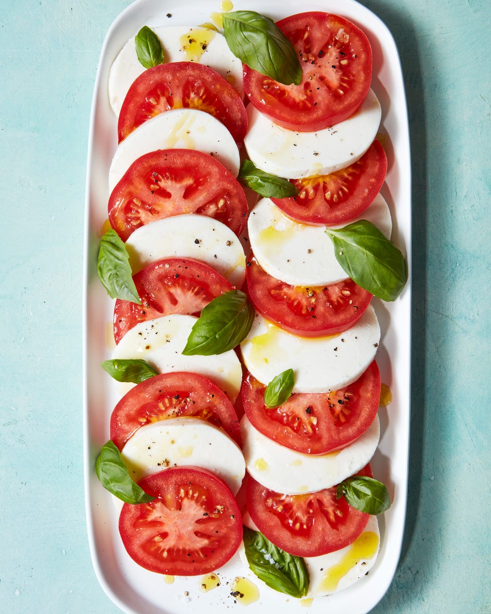 sliced tomatoes, mozzarella, and basil on a plate drizzled with olive oil