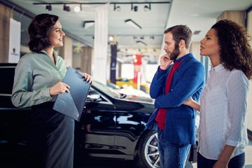 Car dealer is presenting a car to couple in the showroom
