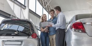 Car dealer showing brochure to young couple in showroom