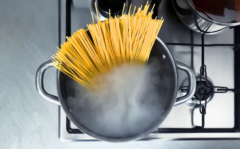cooking raw spaghetti in the boiling water contained in a saucepan italian cuisine raw food interior of a domestic kitchen food preparation and cooking