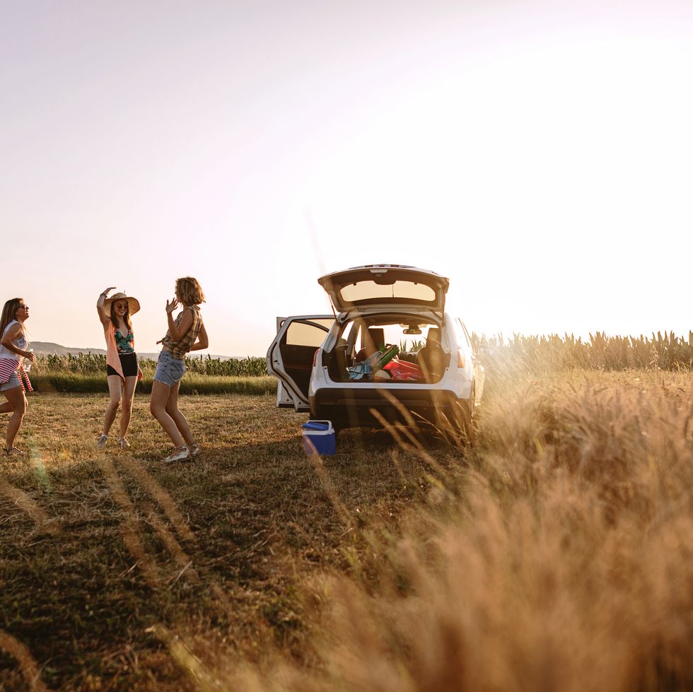 carefree girls dancing behind their car while relaxing from traveling