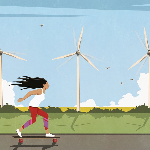 carefree woman skateboarding along wind turbines in sunny field