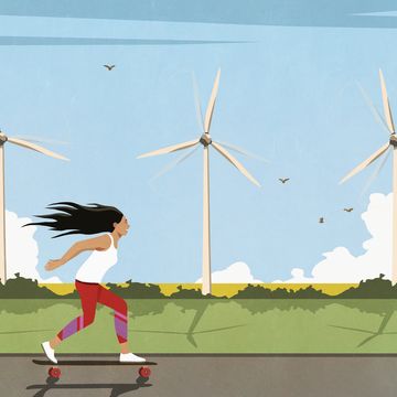 carefree woman skateboarding along wind turbines in sunny field