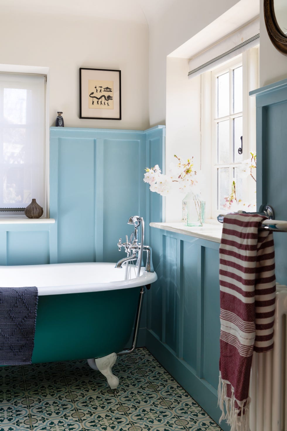 The clawfoot bathtub stands next to the window in the blue bathroom