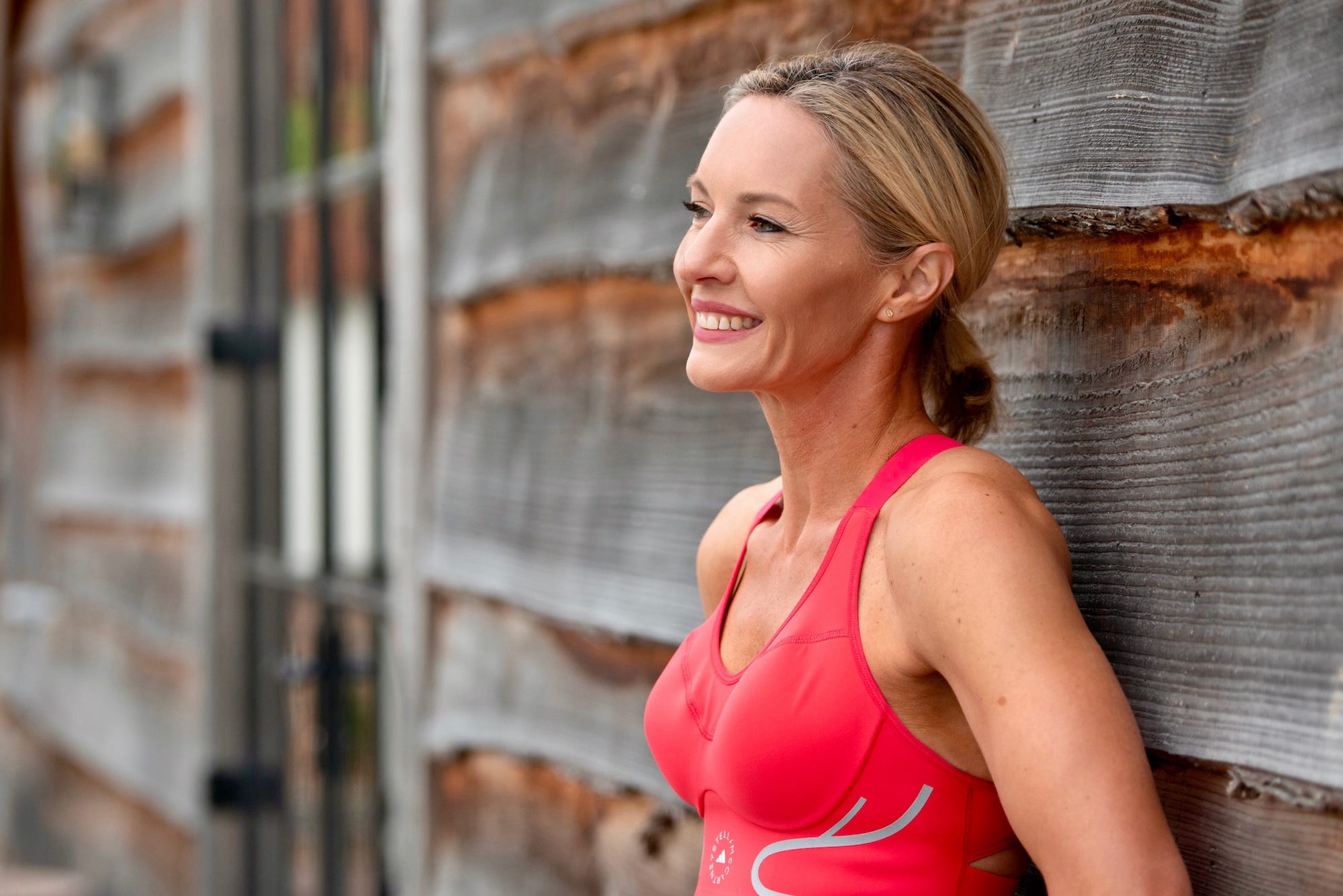 person in athletic wear resting against a wooden wall