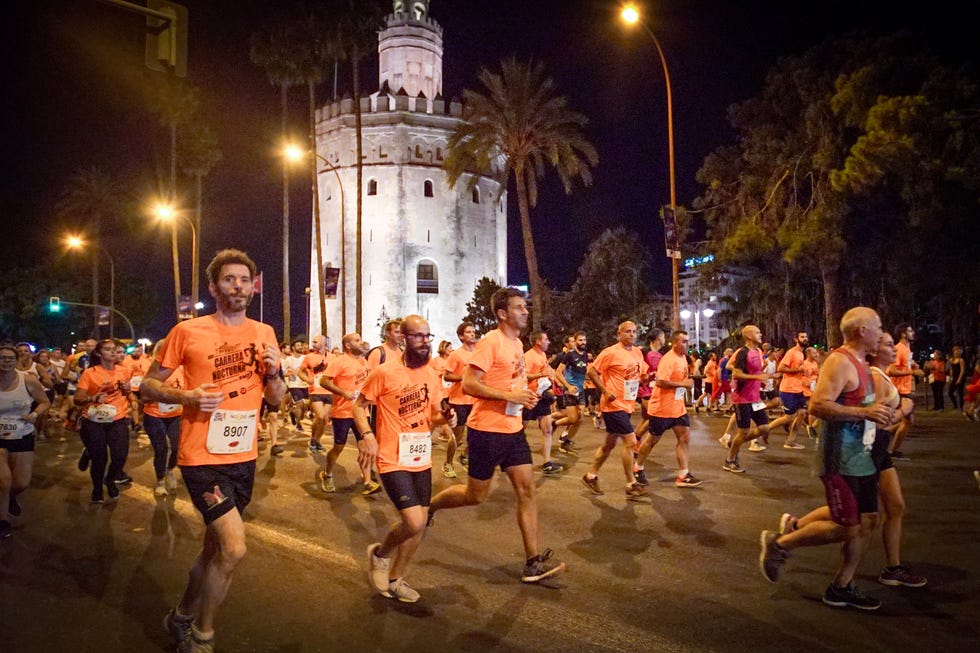 varios corredores pasan por delante de la torre del oro de sevilla en la carrera nocturna del guadalquivir