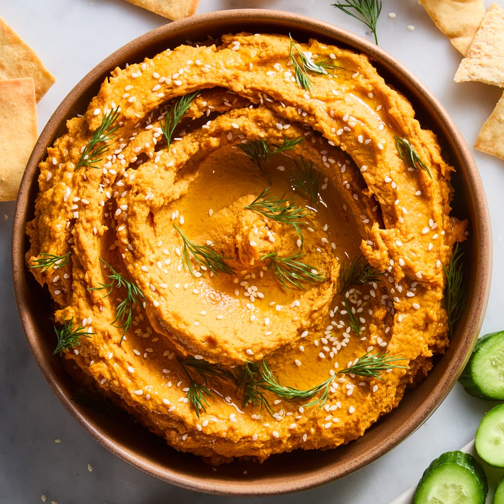 carrot hummus in a bowl with cucumber and pita chips