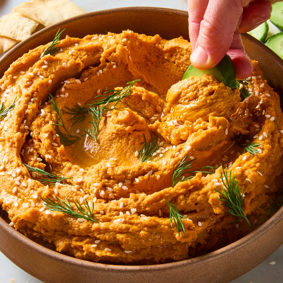 carrot hummus in a bowl with cucumber and pita chips