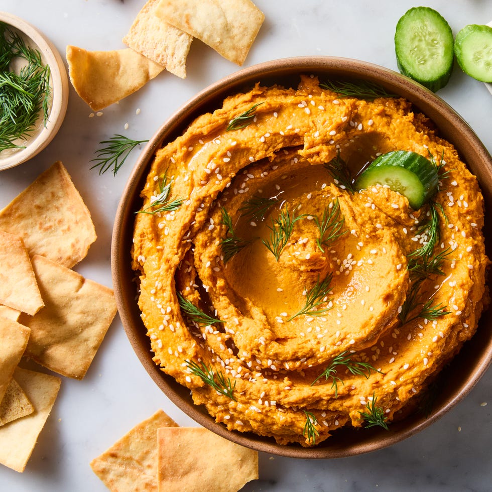 carrot hummus in a bowl with cucumber and pita chips