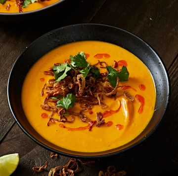 bowl of carrot ginger soup topped with crispy shallots, chili oil, and cilantro