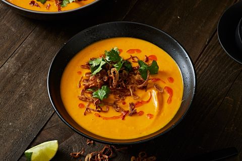 bowl of carrot ginger soup topped with crispy shallots, chili oil, and cilantro