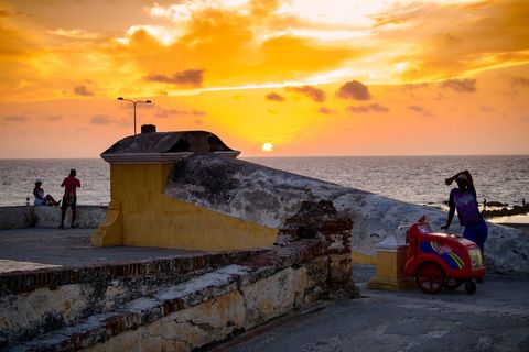 De zon gaat onder boven de baai van Cartagena Colombia een oude en herosche stad die door de schrijver Gabriel Garca Mrquez werd beschreven als de mooiste ter wereld In het zestiendeeeuwse oude centrum van de stad dat in 1984 tot Werelderfgoed werd uitgeroepen vind je romantische balkons monumentale galerijen en uitzichten over de warme Carabische Zee