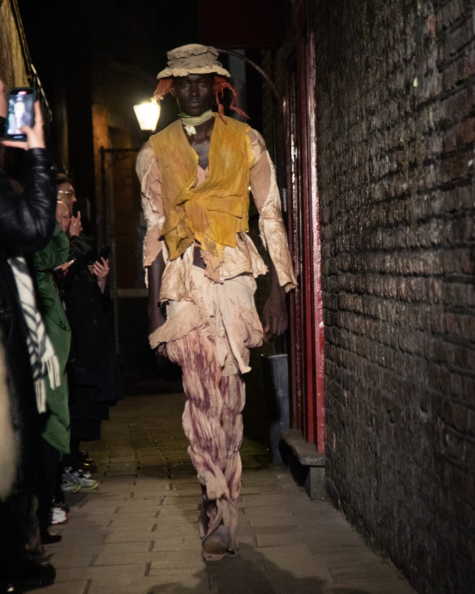 model walking down a narrow alley in a tattered costume