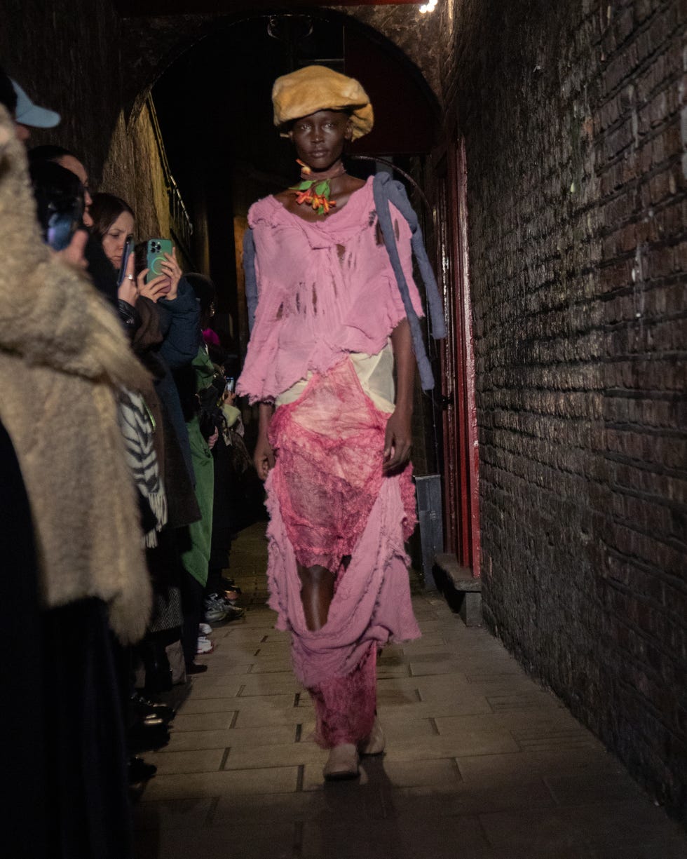 a model showcases a unique clothing design in a narrow alley during a fashion event