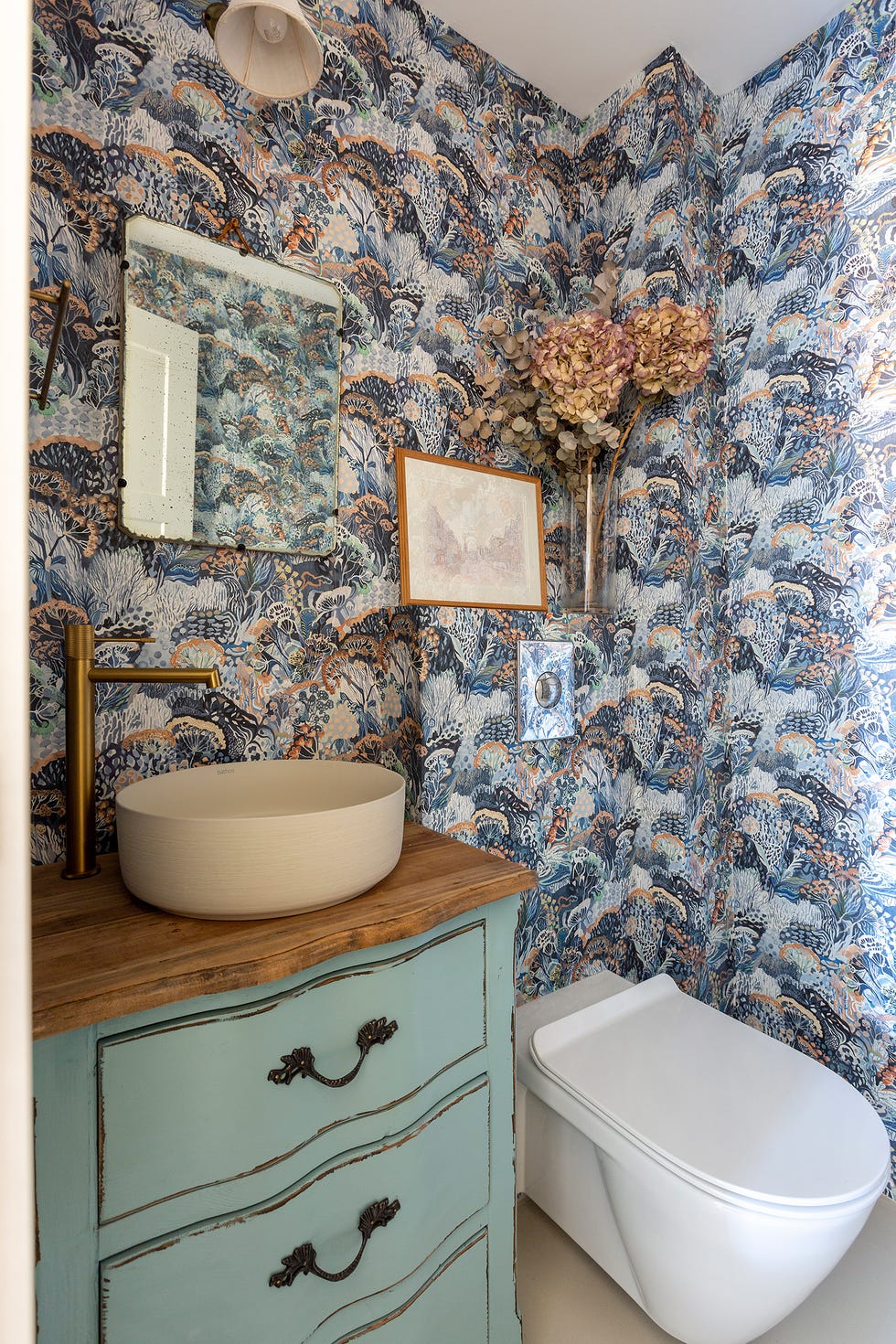 baño con papel pintado colorido y mueble vintage de madera