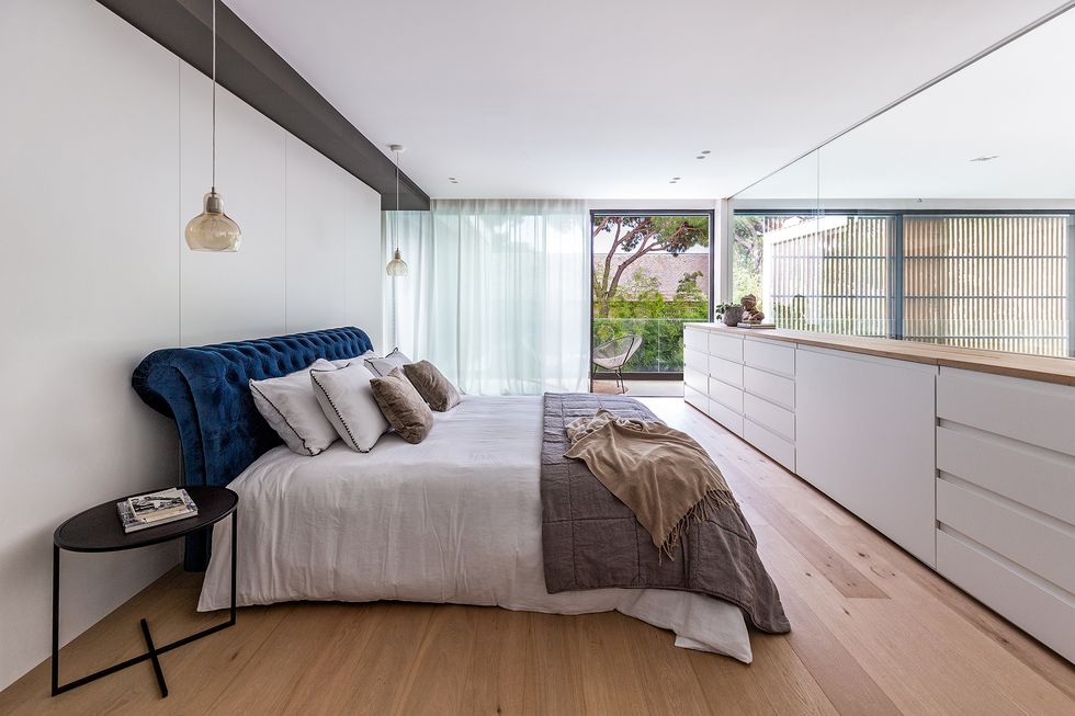 dormitorio decorado en blanco con muebles a medida y cabecero de terciopelo azul capitoné