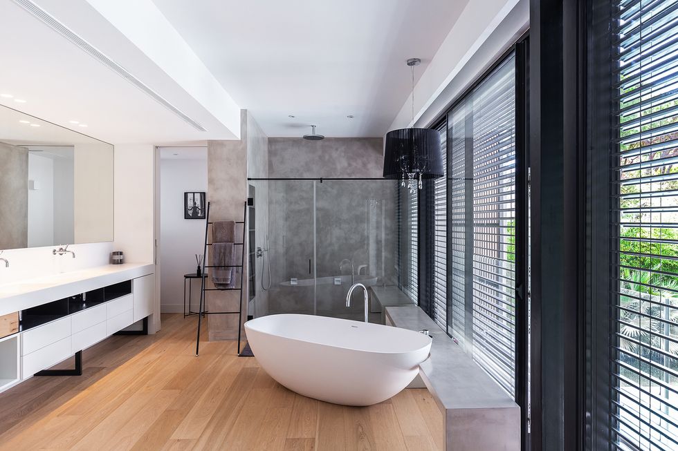 baño con paredes de microcemento gris, suelo de madera y bañera exenta