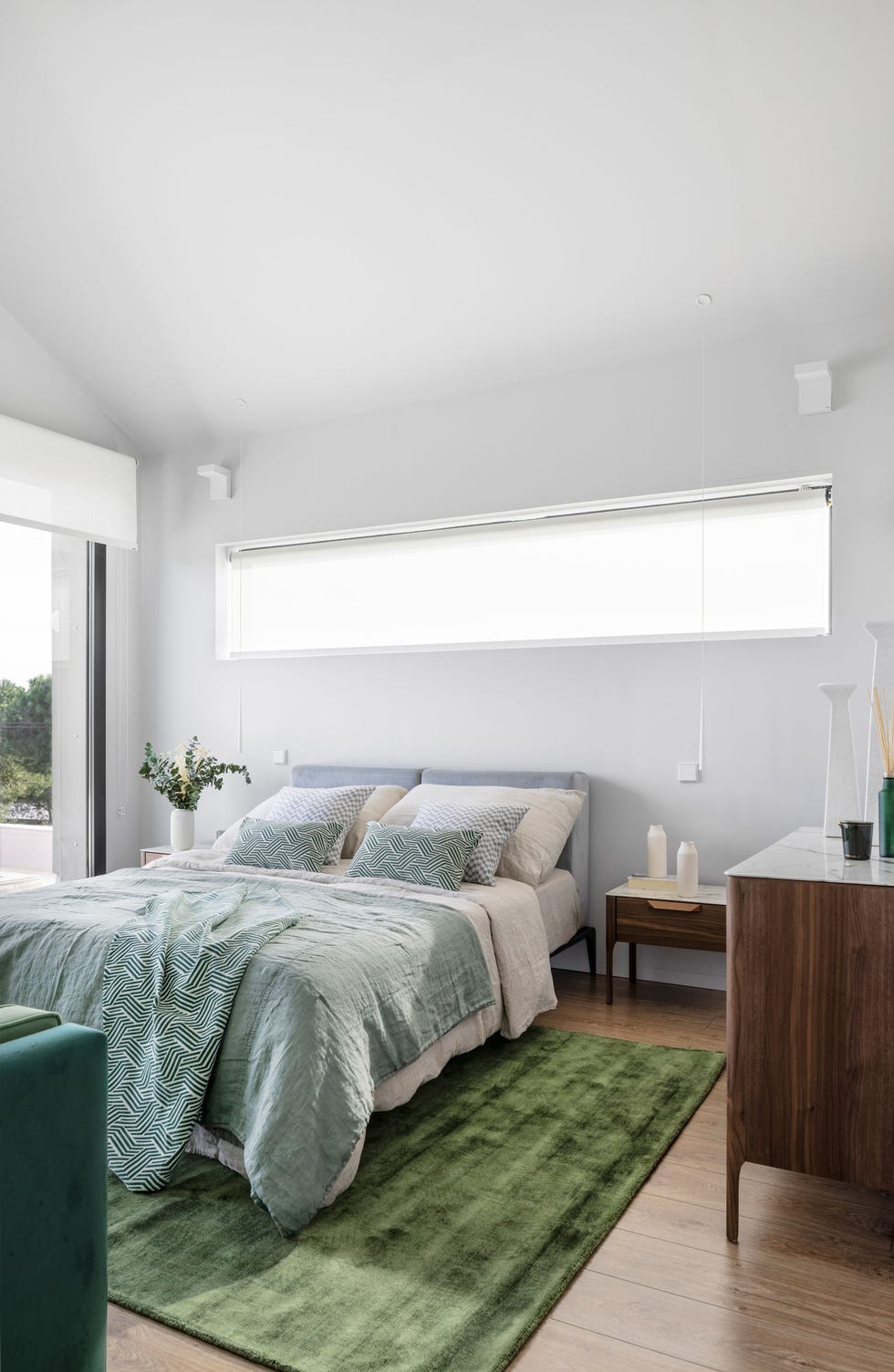 dormitorio abuhardillado con cama con cabecero tapizado en gris y muebles de madera con tapa de mármol