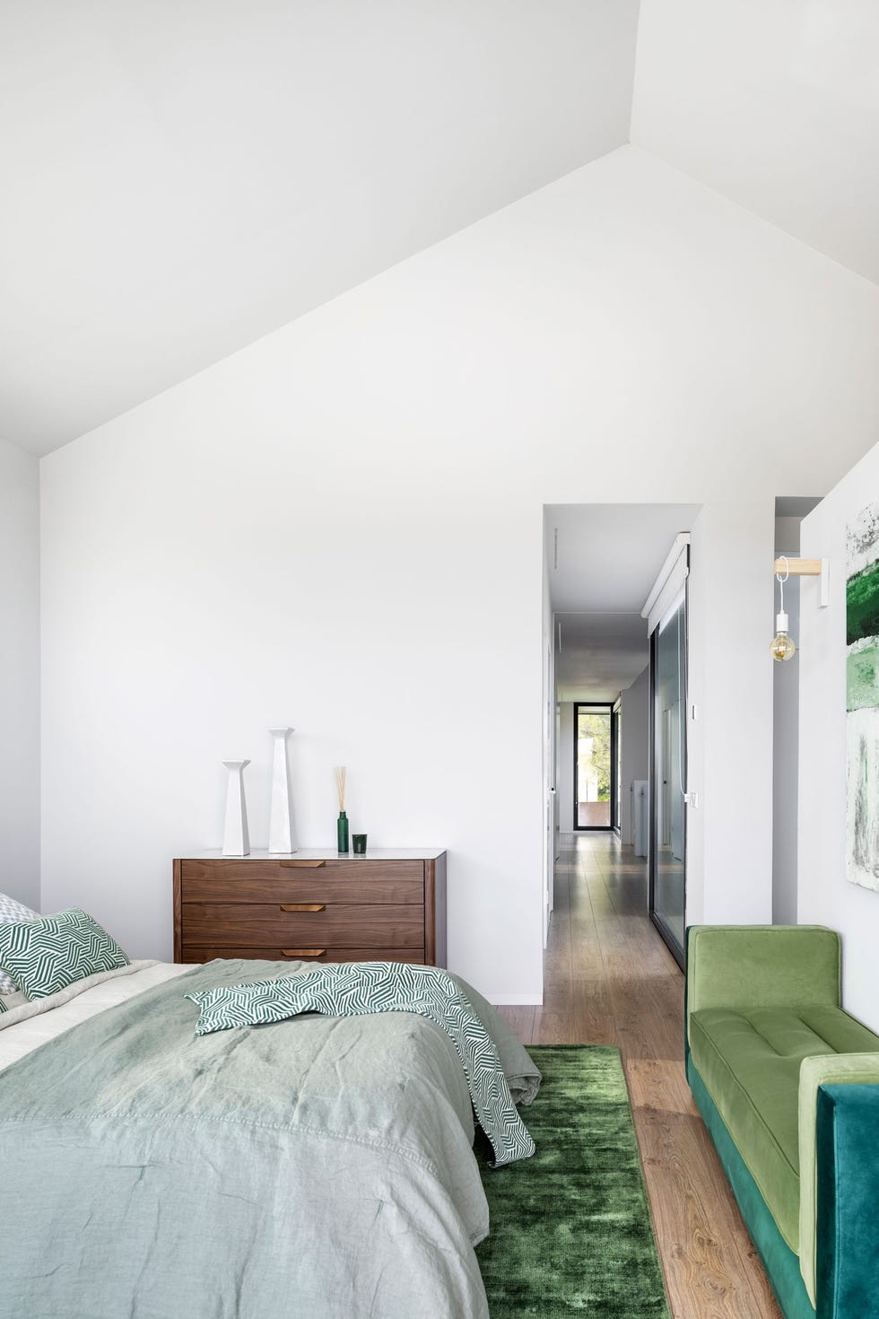 dormitorio abuhardillado con banco de terciopelo verde a los pies y cómoda de madera con tapa de mármol