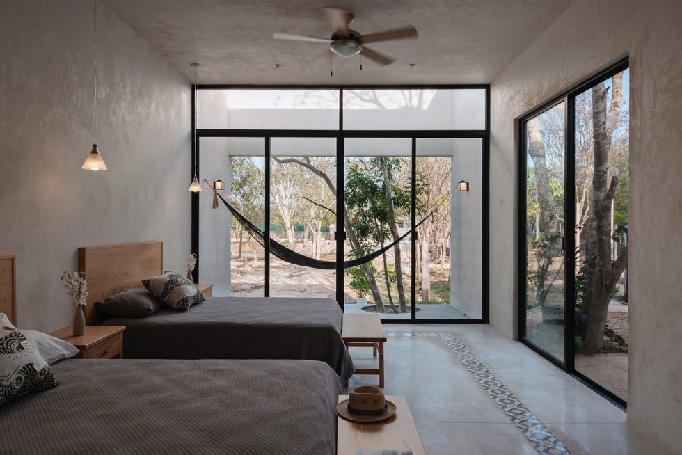 dormitorio con camas y bancos de madera, paredes y suelo de microcemento y puertas correderas con acceso a la terraza