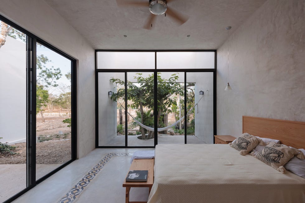 dormitorio con cama y banco de madera, paredes y suelo de microcemento y puertas correderas con acceso a la terraza