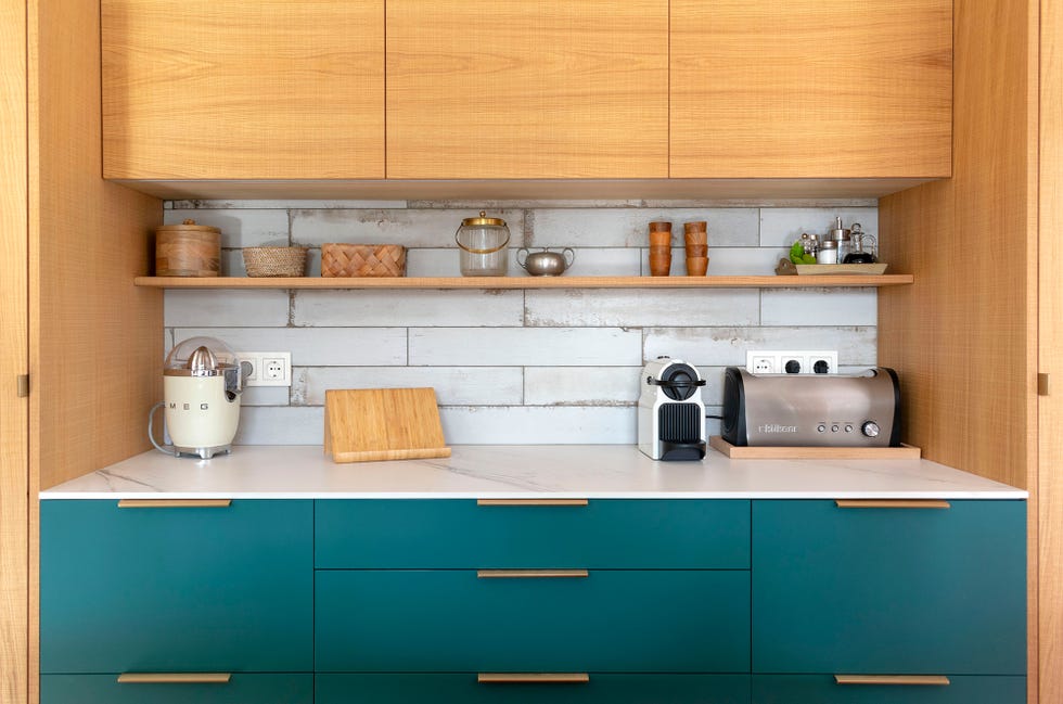 cocina con armarios superiores de madera, frente de azulejos, y armarios inferiores con acabado en color esmeralda