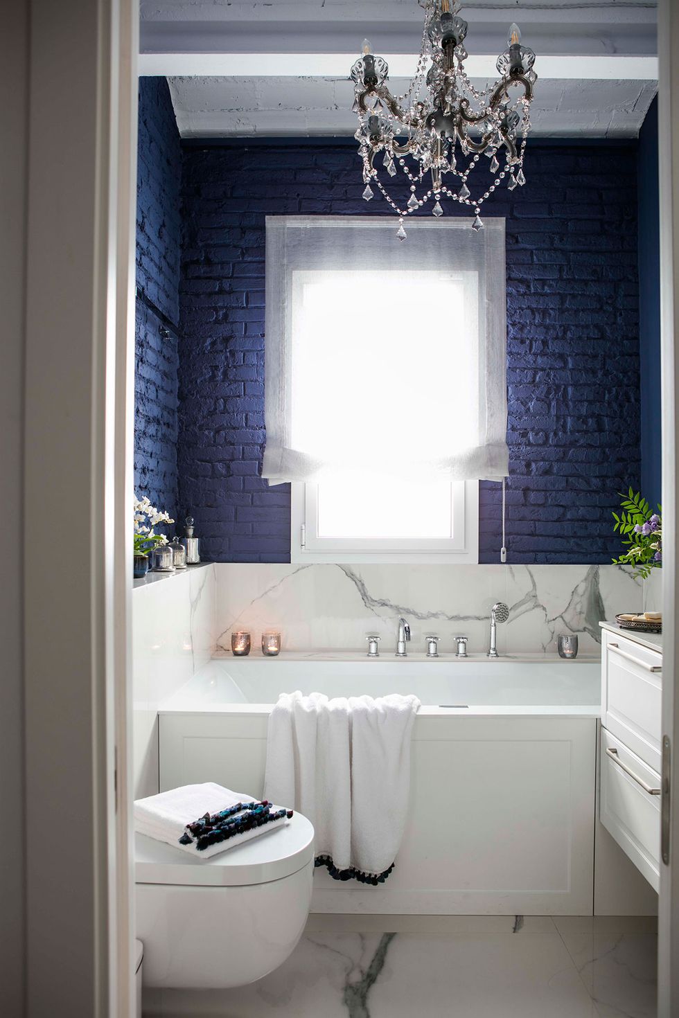 baño pintado en azul con bañera y lámpara de araña