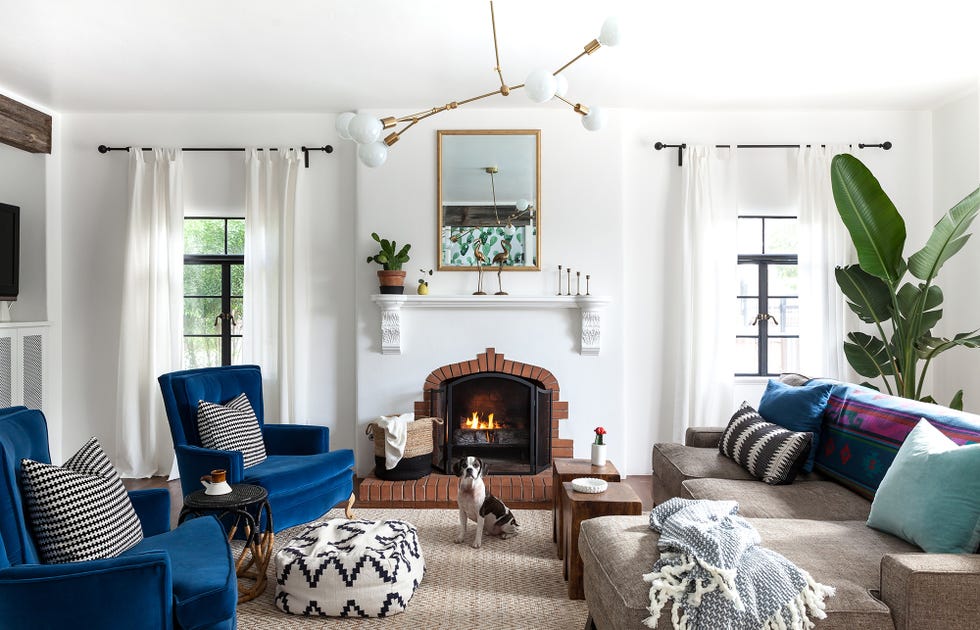 salón con chimenea de piedra, dos butacas de terciopelo azul, un sofá gris y una lámpara de techo mid century