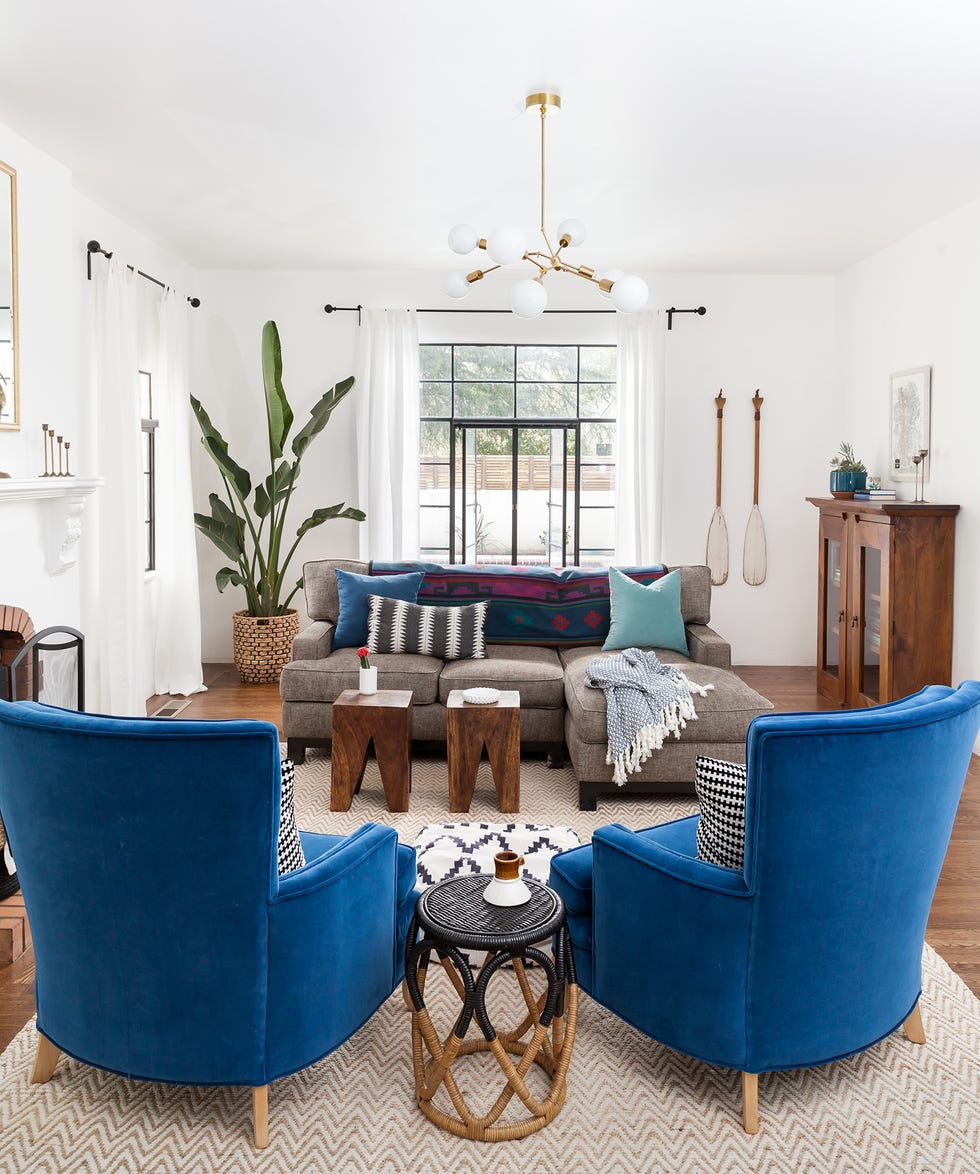 salón con chimenea de piedra, dos butacas de terciopelo azul, un sofá gris y una lámpara de techo mid century